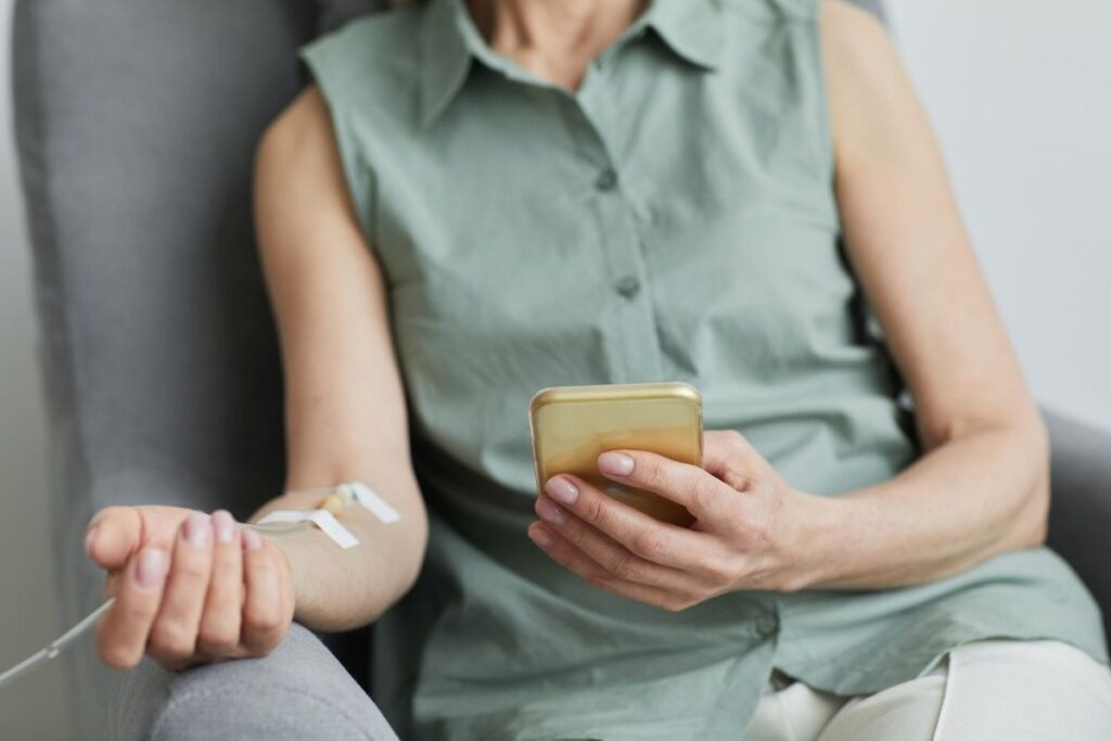 Patient comfortably using a smartphone while receiving IV Therapy for Hydration treatment.